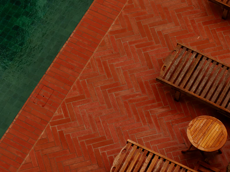 Brick pavers laid in herringbone at a pool edge with wooden loungers